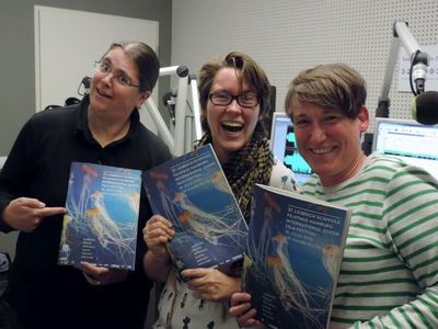 Zwei Radiomoderatorinnen und ein Teammitglied lachend im Radiostudio, die Programmhefte 2016 haltend